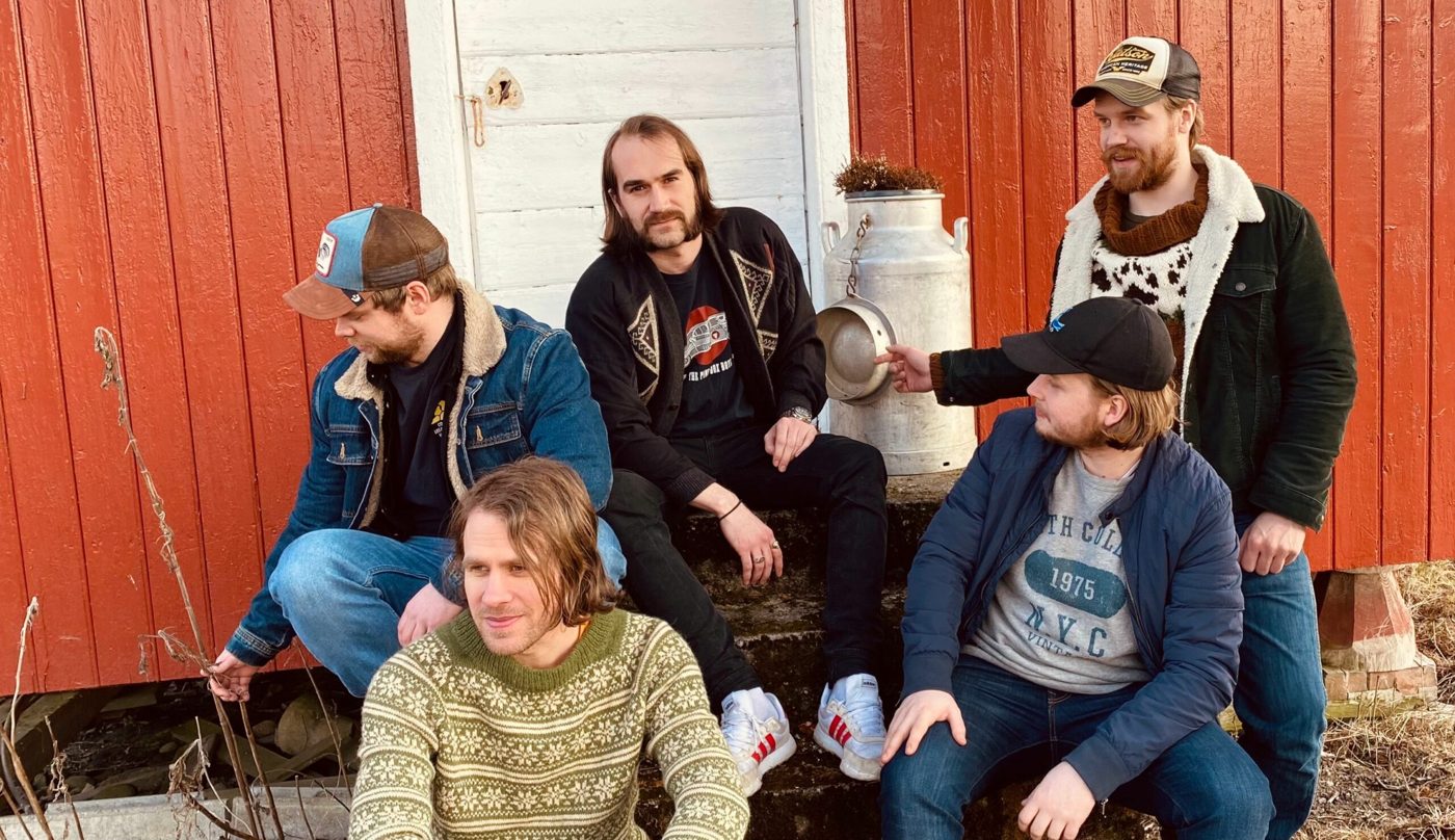 Johan og Trøgstad Musikkompani foran en rød låvevegg.